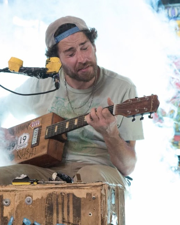 The same performer leaning into his playing, backlit by dense white stage smoke